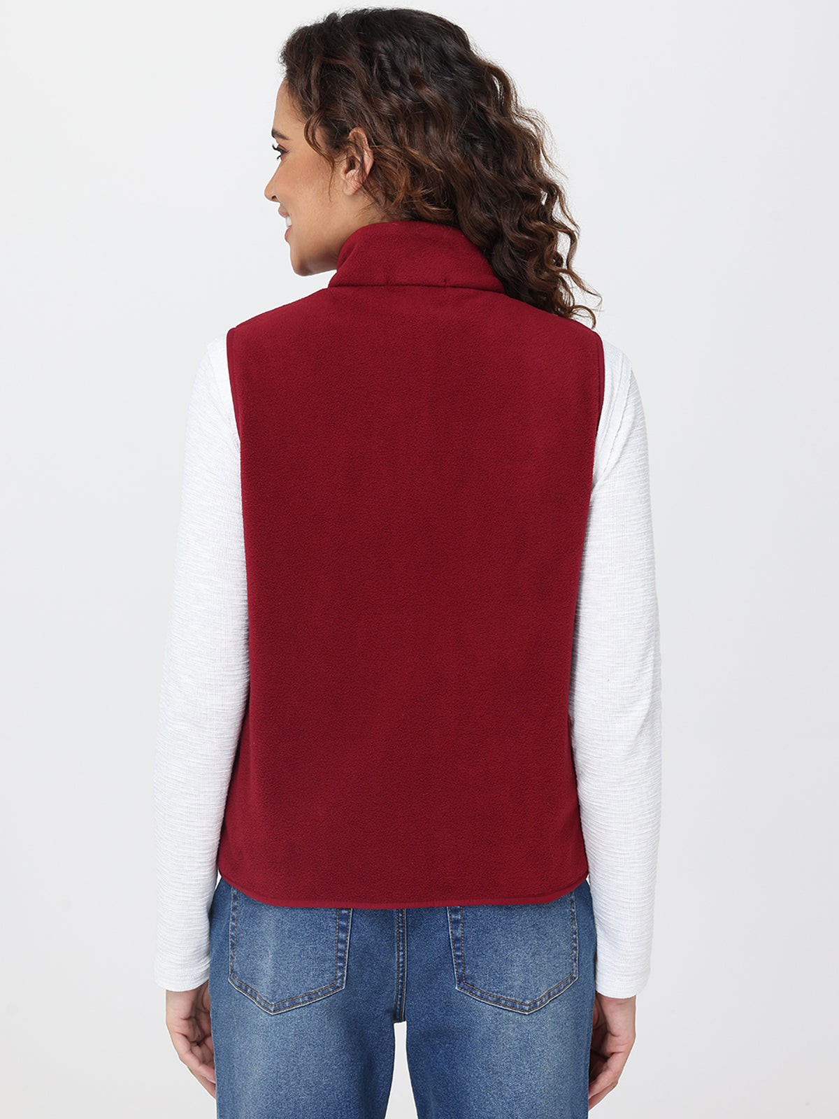 Person wearing a red vest over a white shirt and blue jeans on a light gray background