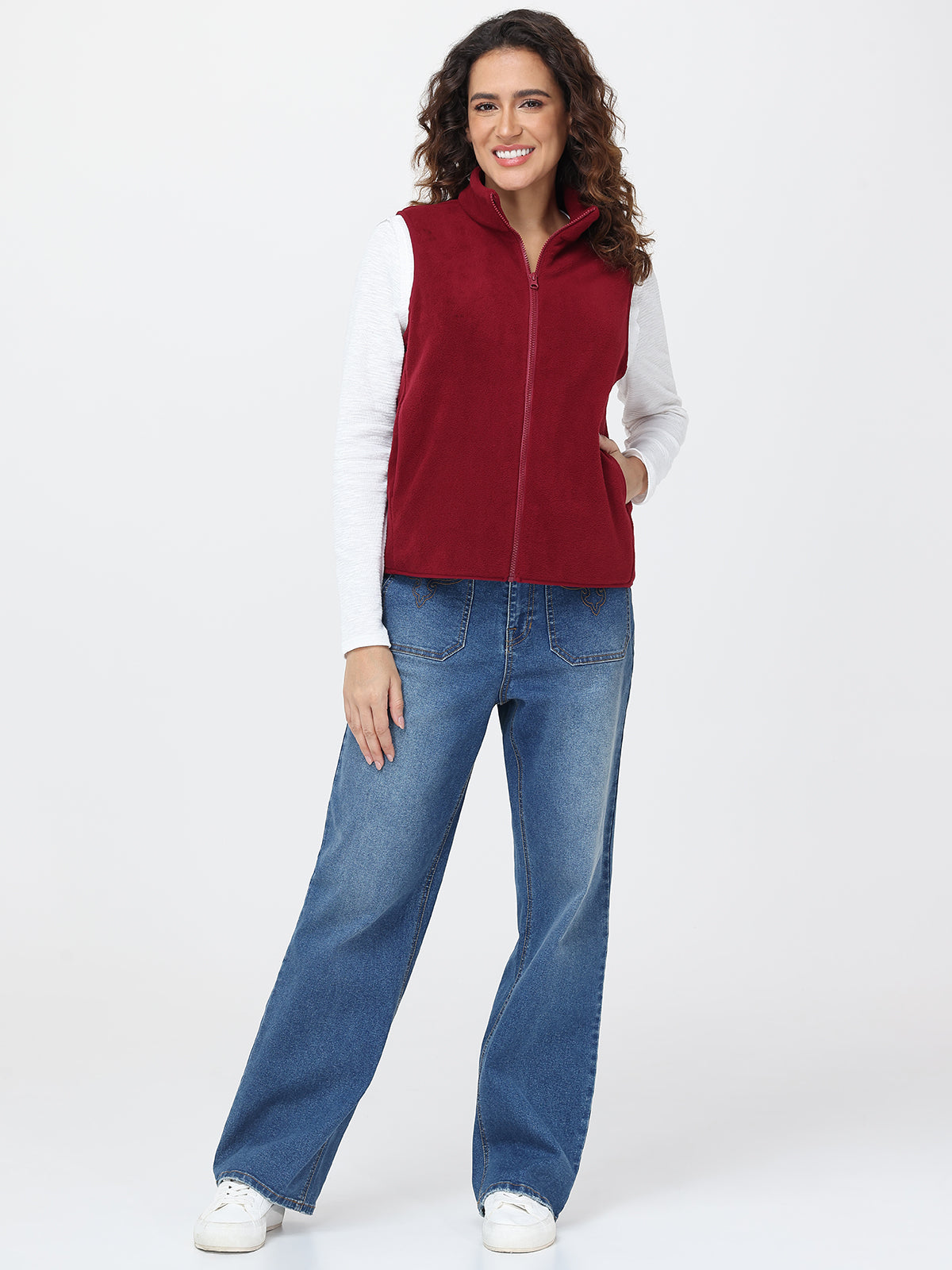 Woman wearing a red vest and blue jeans on a white background