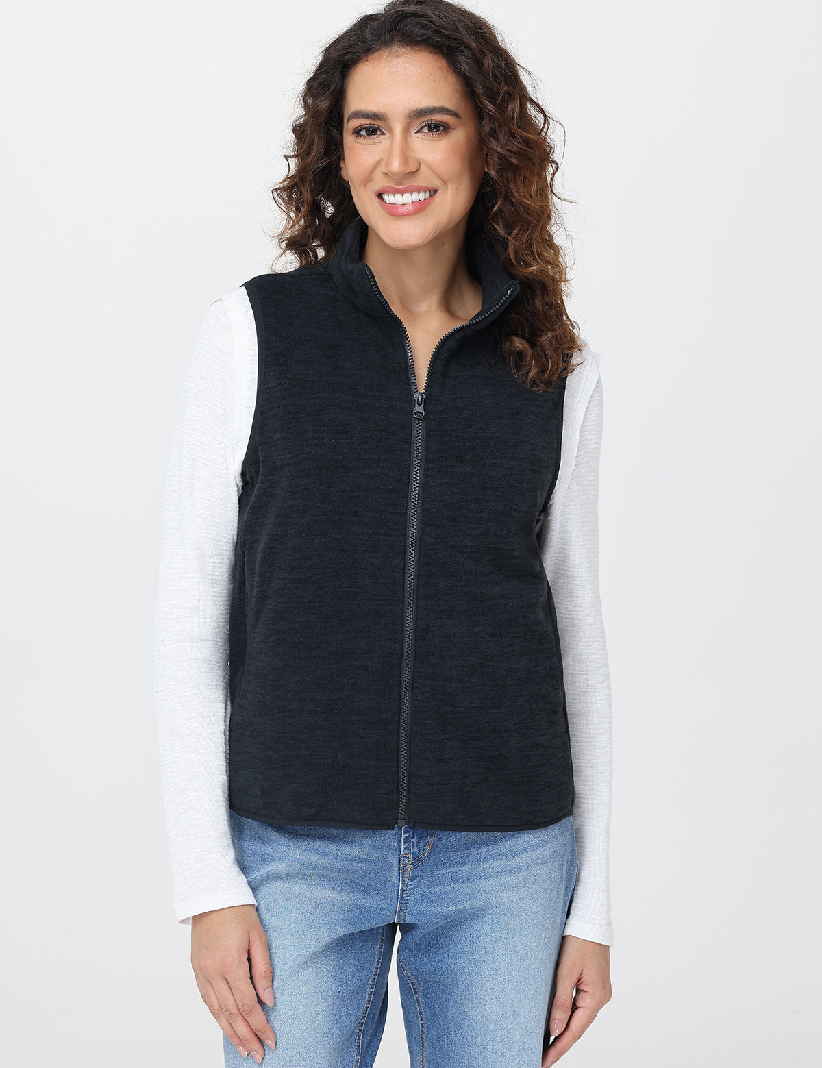 Woman wearing a black vest over a white shirt with a plain background