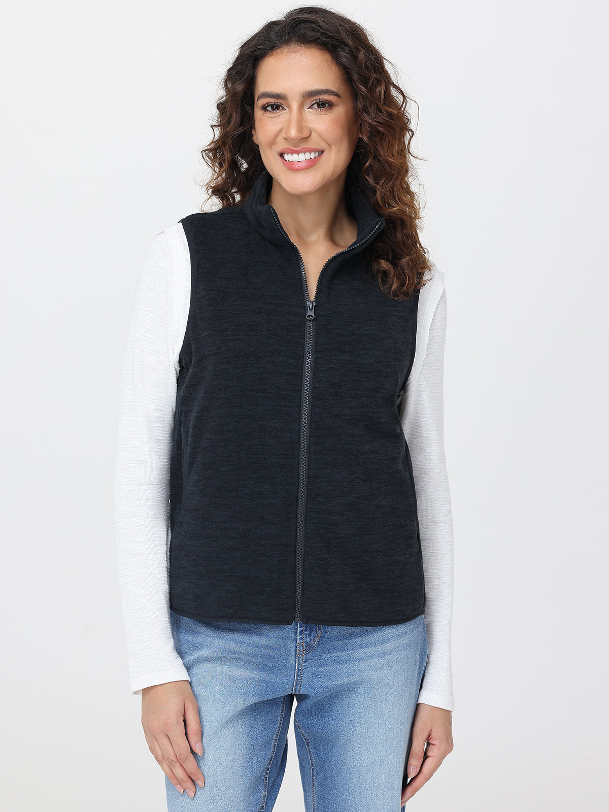 Woman wearing a black vest over a white shirt with a plain background