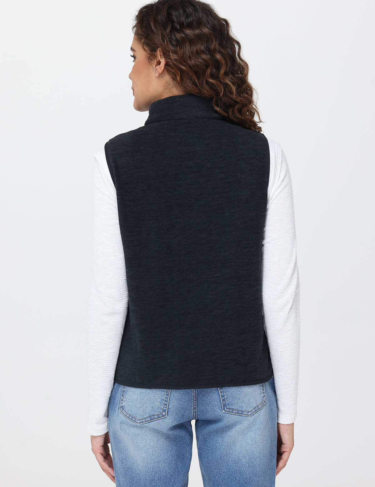 Person wearing a navy vest over a white shirt and blue jeans on a light gray background