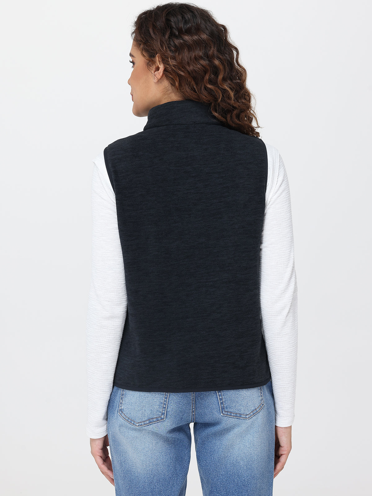 Person wearing a navy vest over a white shirt and blue jeans on a light gray background