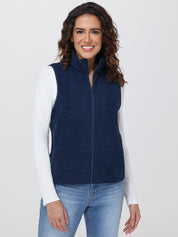 Woman wearing a navy blue vest over a white long-sleeve shirt and blue jeans on a light gray background