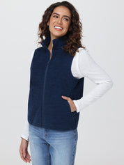 Woman wearing a navy blue vest over a white long-sleeve shirt on a light gray background