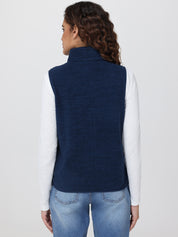 Person wearing a navy blue vest over a white shirt and blue jeans on a light gray background