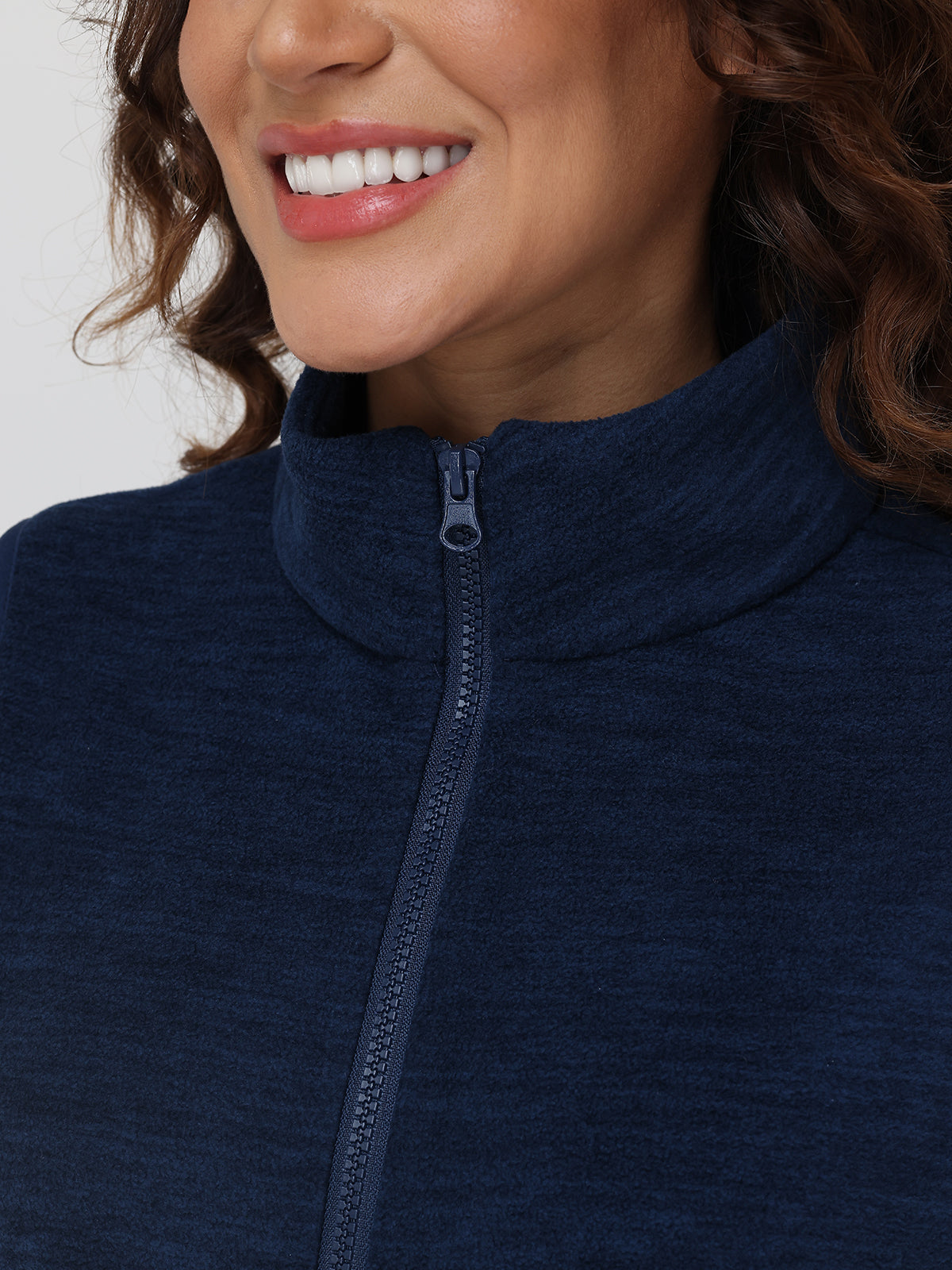 Close-up of a person wearing a navy blue zip-up sweatshirt with a plain background