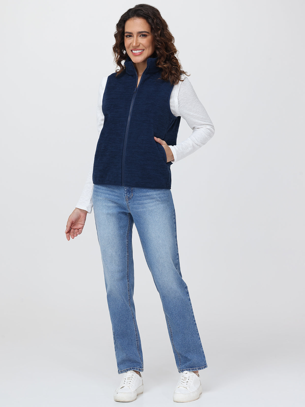 Woman wearing a navy blue vest over a white shirt with light blue jeans on a white background