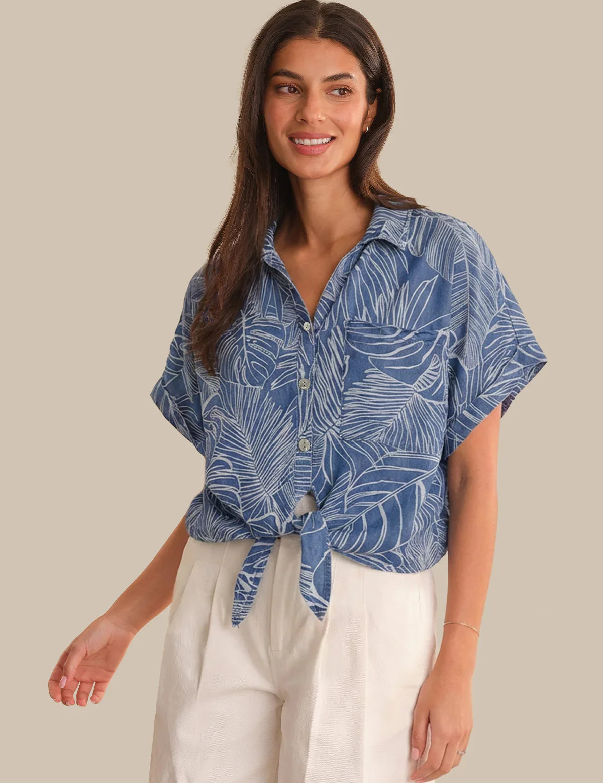 Woman wearing a blue leaf-patterned shirt with white pants on a beige background