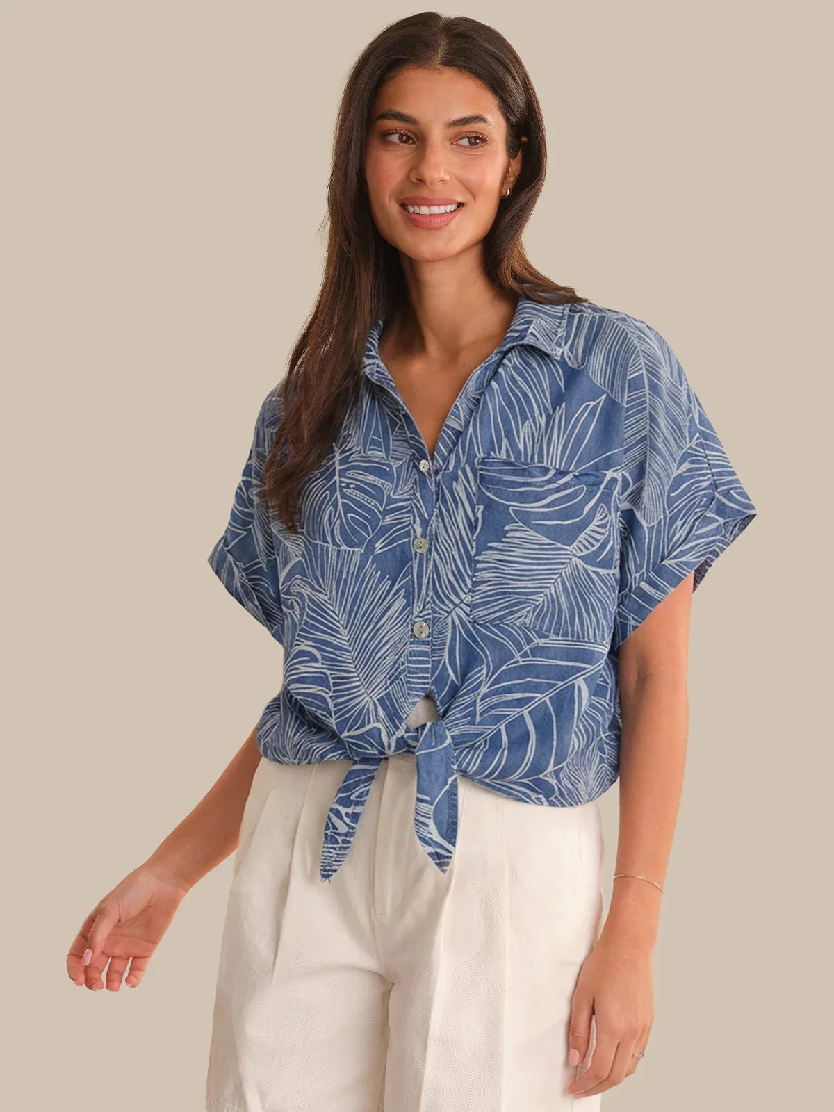Woman wearing a blue leaf-patterned shirt with white pants on a beige background