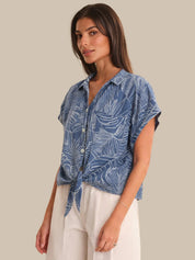 Woman wearing a blue leaf-patterned shirt against a beige background