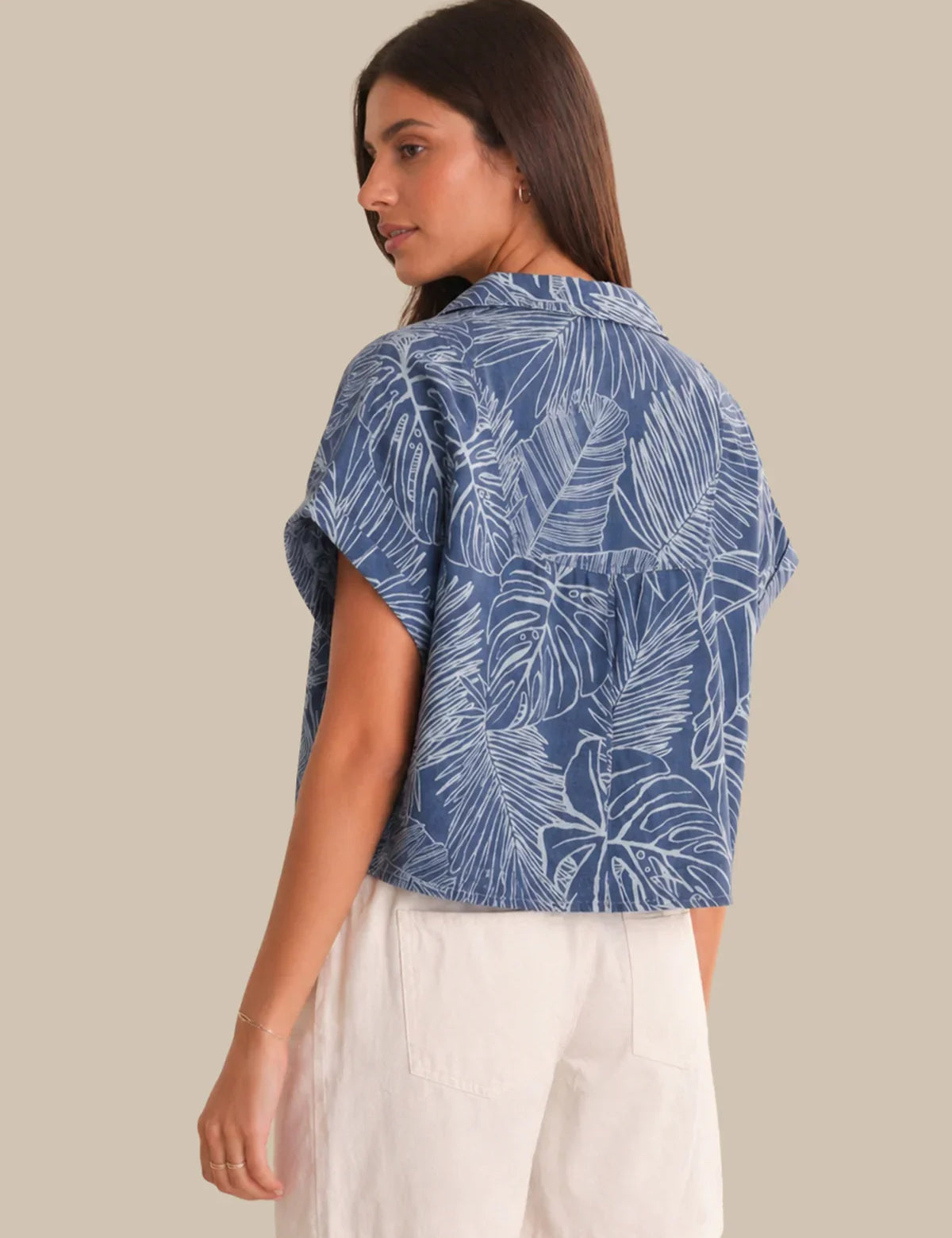 Woman wearing a blue leaf-patterned shirt with white pants on a beige background