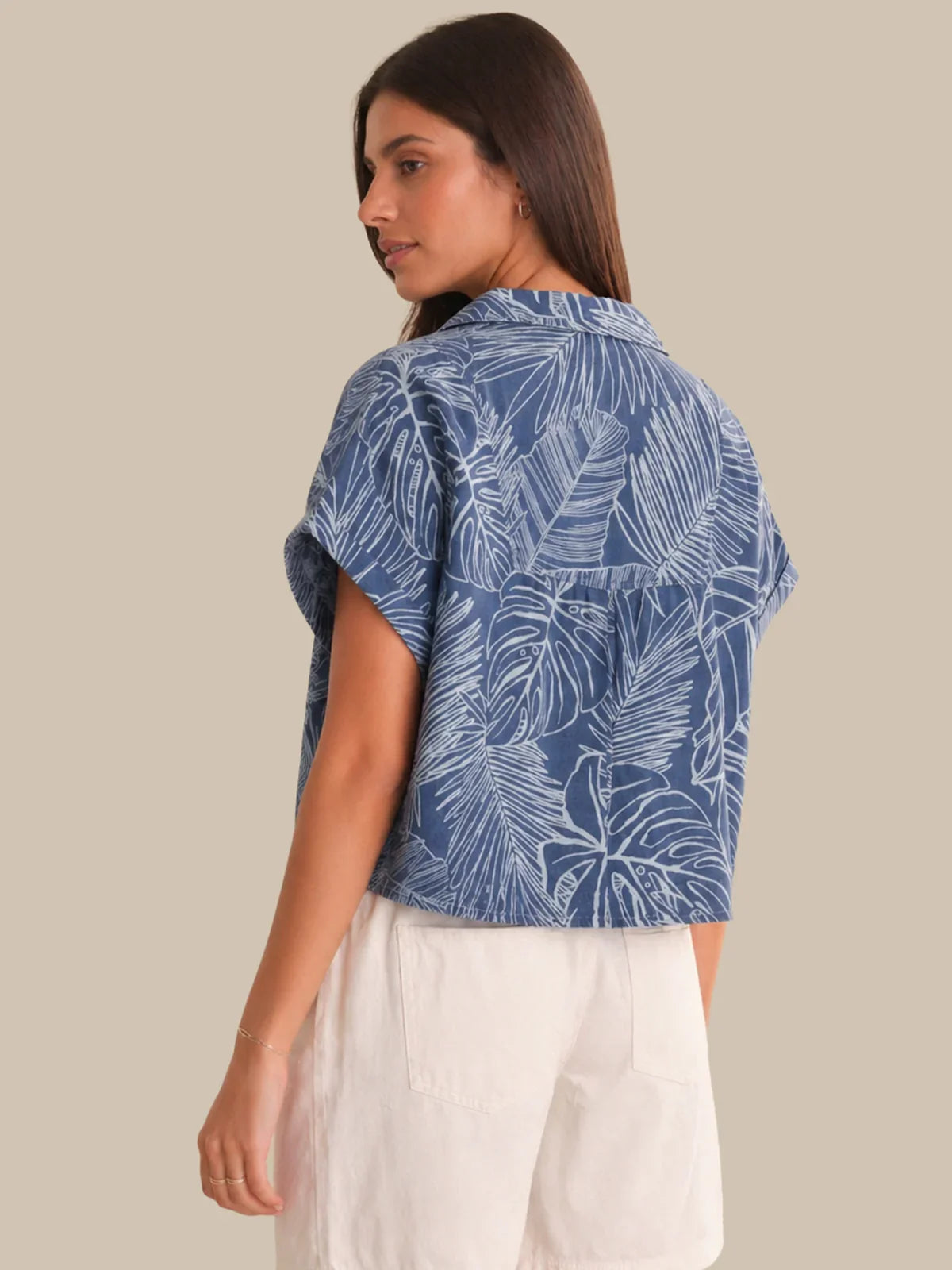 Woman wearing a blue leaf-patterned shirt with white pants on a beige background