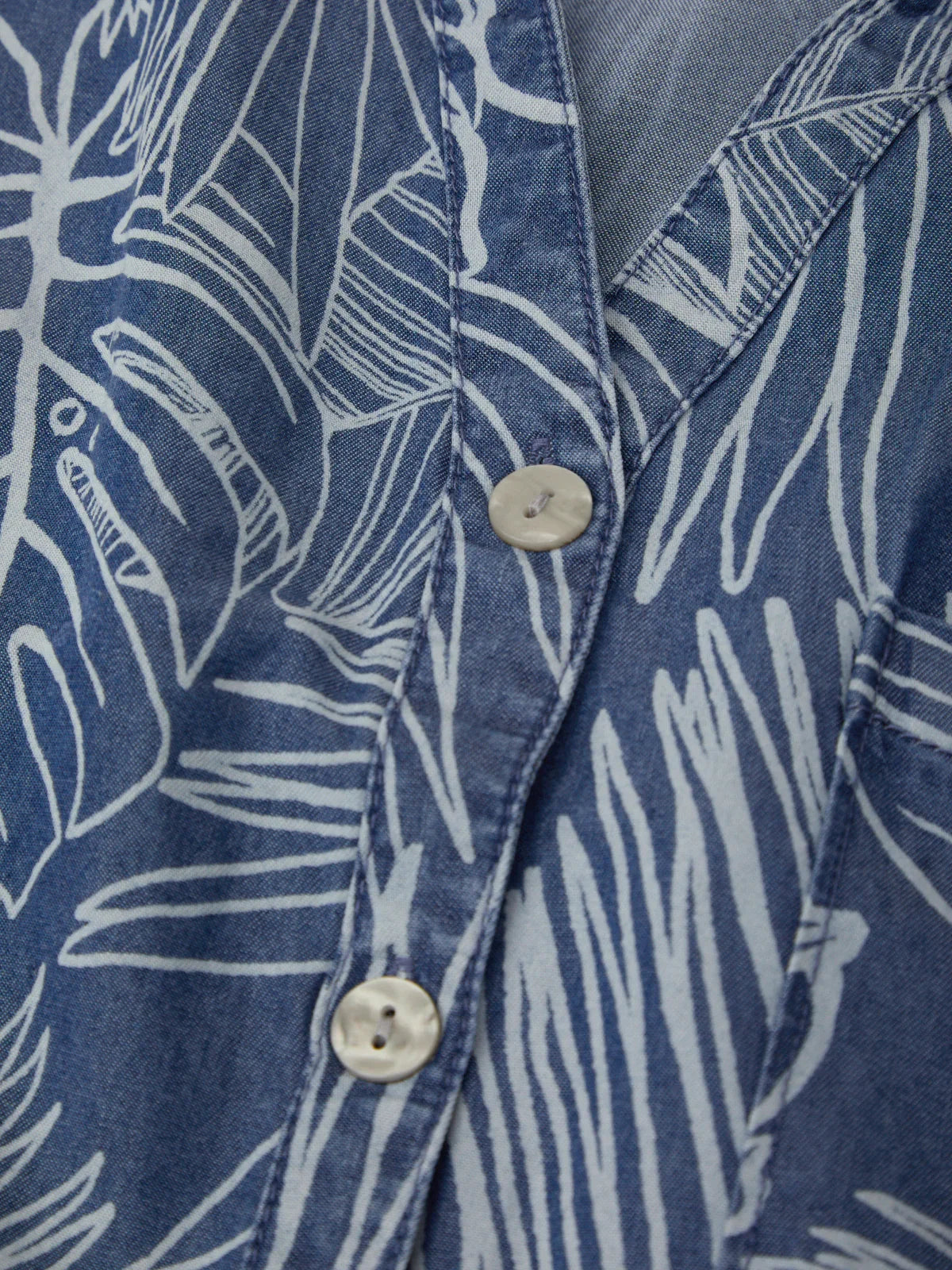 Close-up of a blue shirt with white leaf pattern and button details.