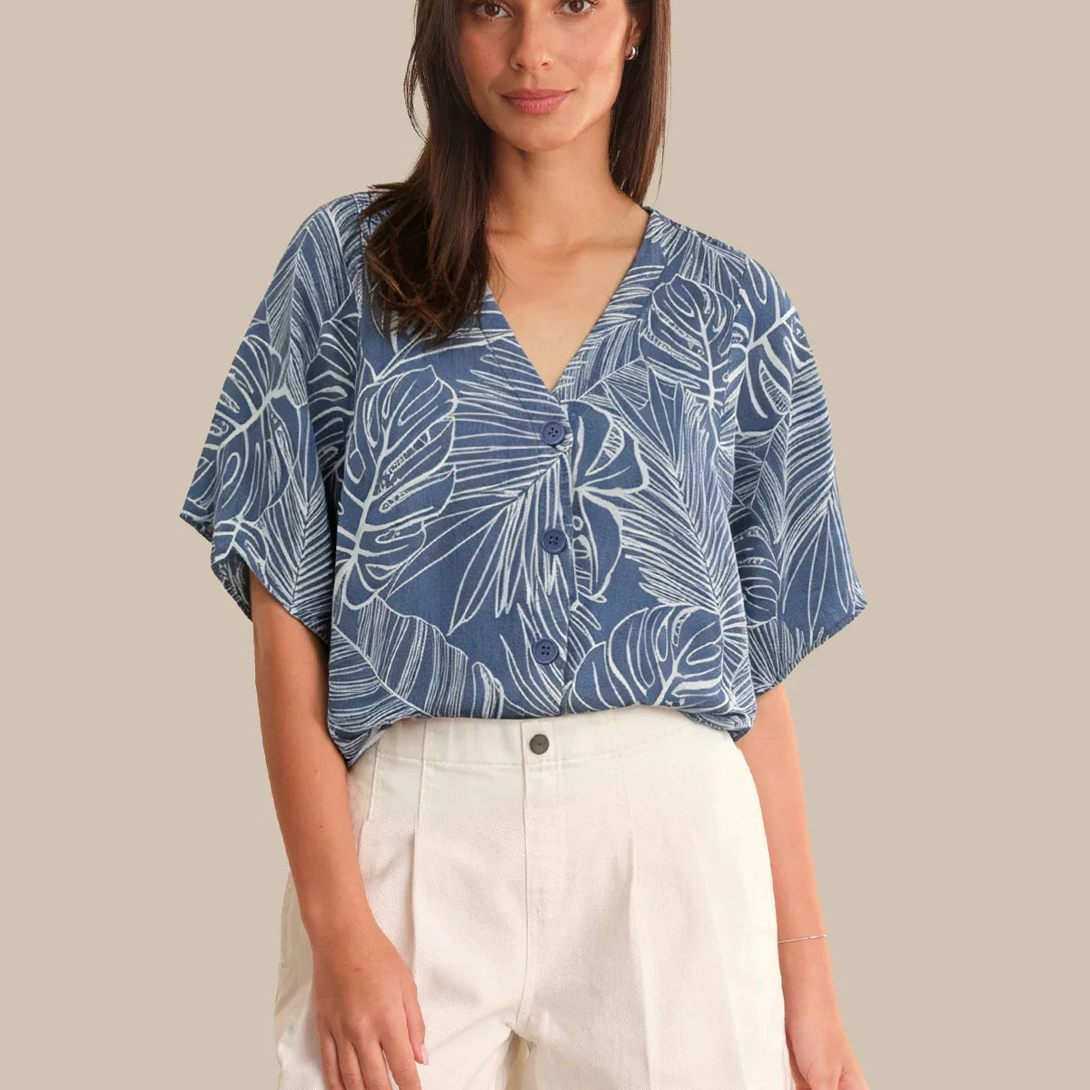 Woman wearing a blue leaf-patterned top and white shorts on a beige background