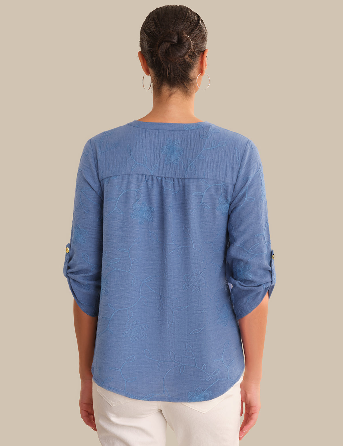 Person wearing a blue shirt with rolled-up sleeves on a beige background