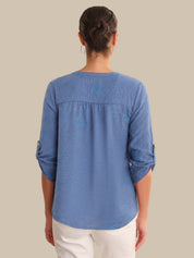 Person wearing a blue shirt with rolled-up sleeves on a beige background