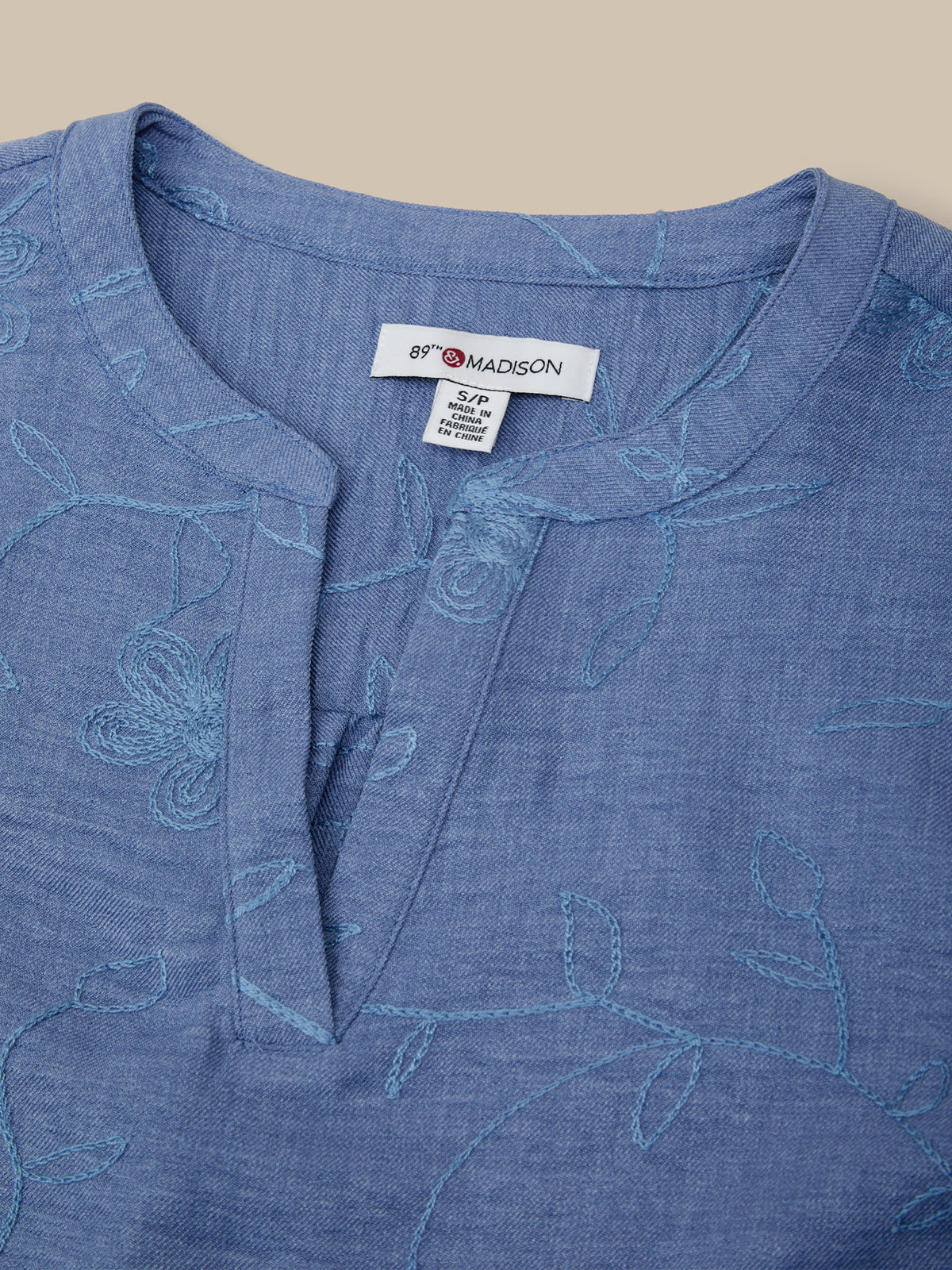Blue embroidered shirt with 'Brooke Madison' label on a beige background