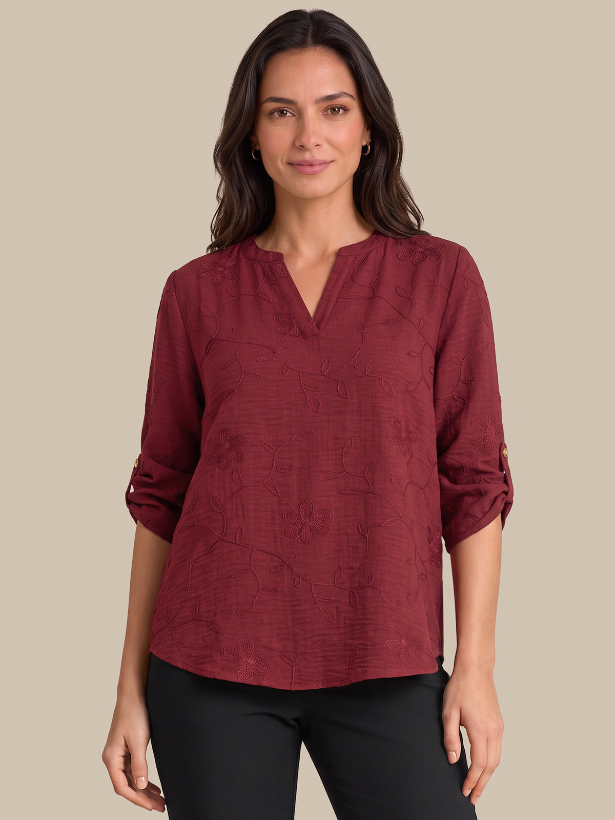 A woman modeling a burgundy long-sleeve blouse with a split V-neckline and subtle tonal textured pattern, paired with black pants, against a solid beige background.
