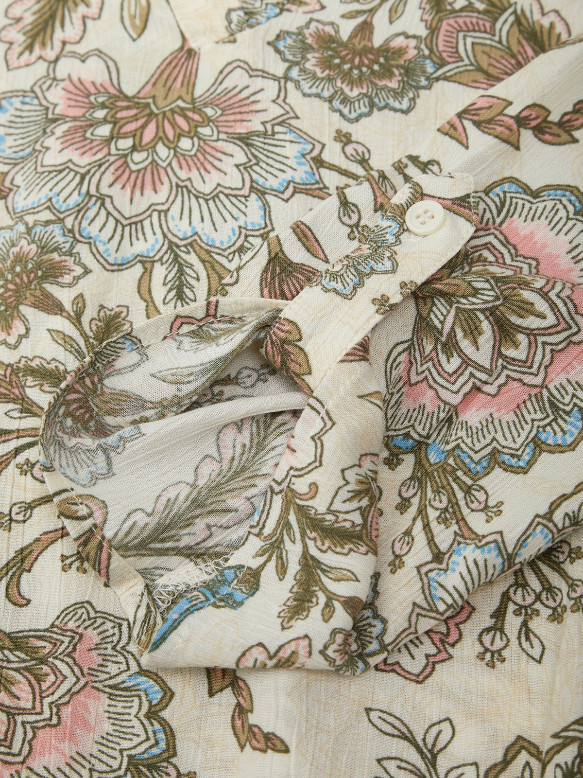 Close-up of a floral patterned fabric with pink, blue, and green colors on a beige background.