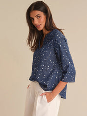 Woman wearing a blue blouse with star pattern and white pants on a beige background