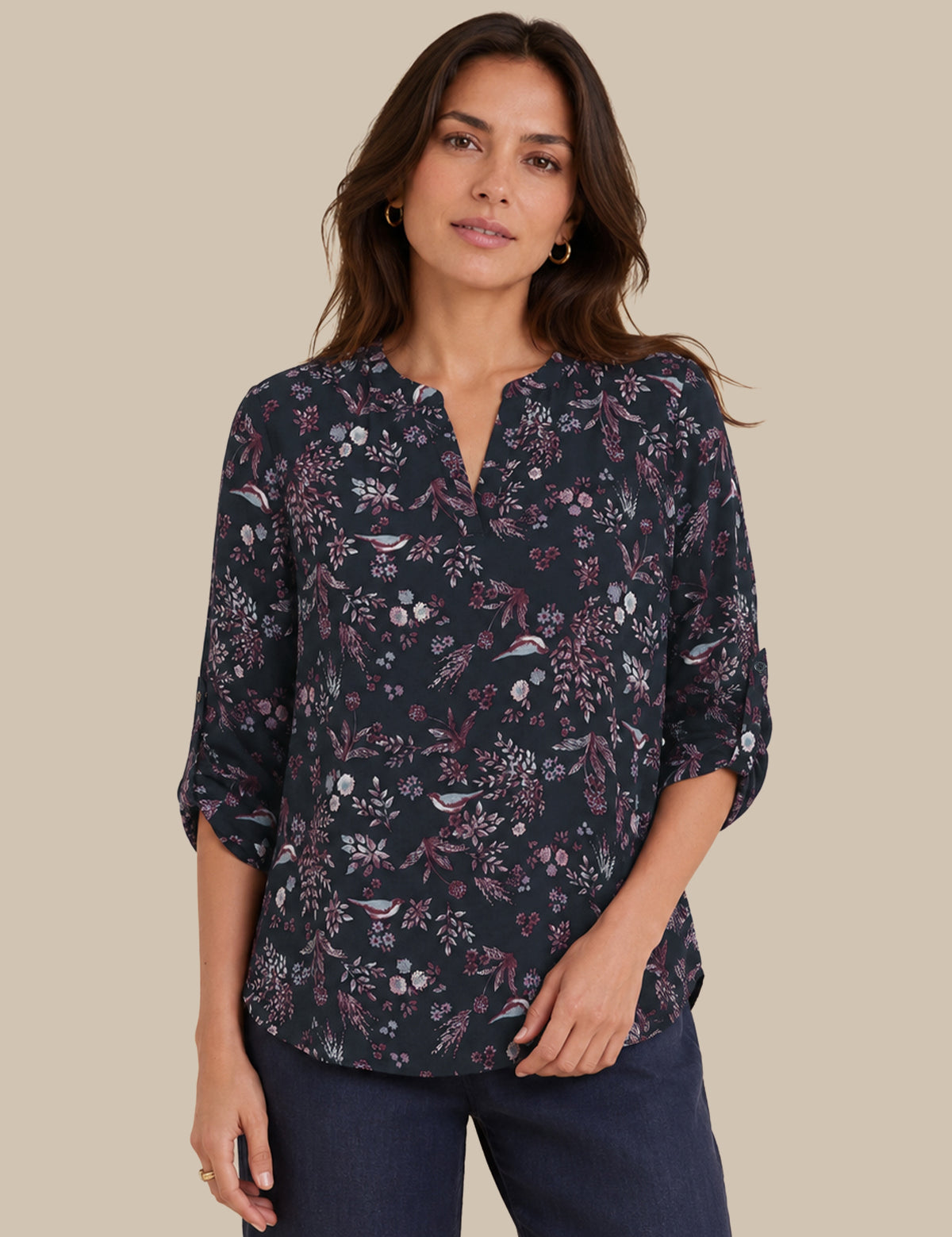 A woman modeling a dark navy floral blouse with a split neckline and three-quarter sleeves, paired with dark blue jeans, against a solid beige background.