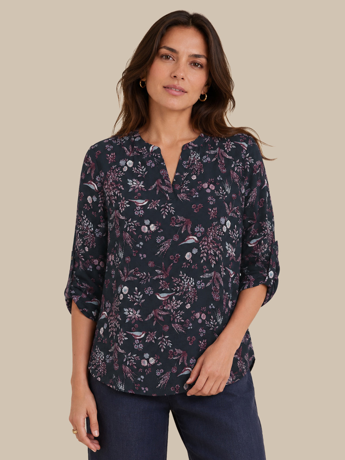 A woman modeling a dark navy floral blouse with a split neckline and three-quarter sleeves, paired with dark blue jeans, against a solid beige background.