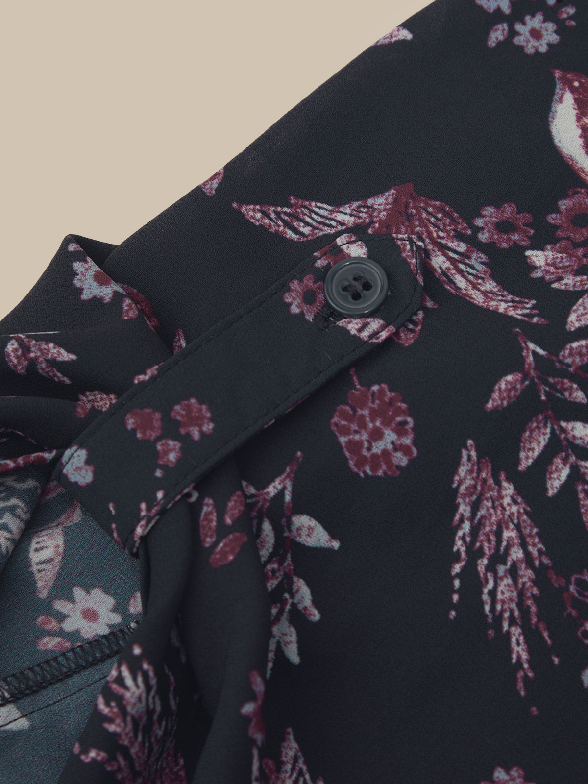 Close-up of a dark floral garment detail showing a button closure, fabric texture, and a pink and white botanical print on a black base.