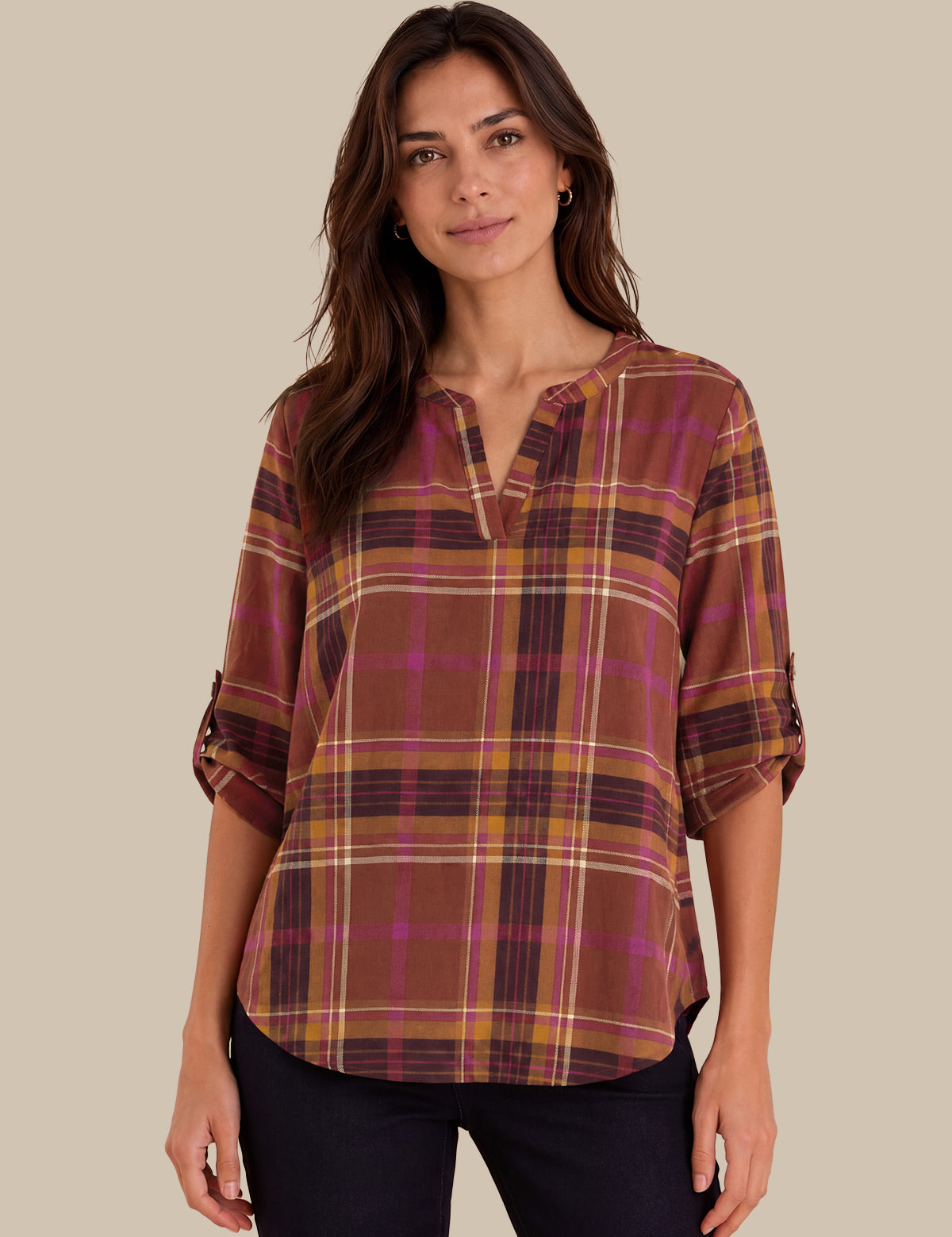 A woman modeling a brown plaid blouse with purple and yellow stripes, featuring a split neckline and rolled sleeves, set against a solid beige background.