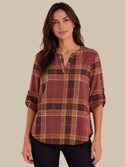 A woman modeling a brown plaid blouse with purple and yellow stripes, featuring a split neckline and rolled sleeves, set against a solid beige background.