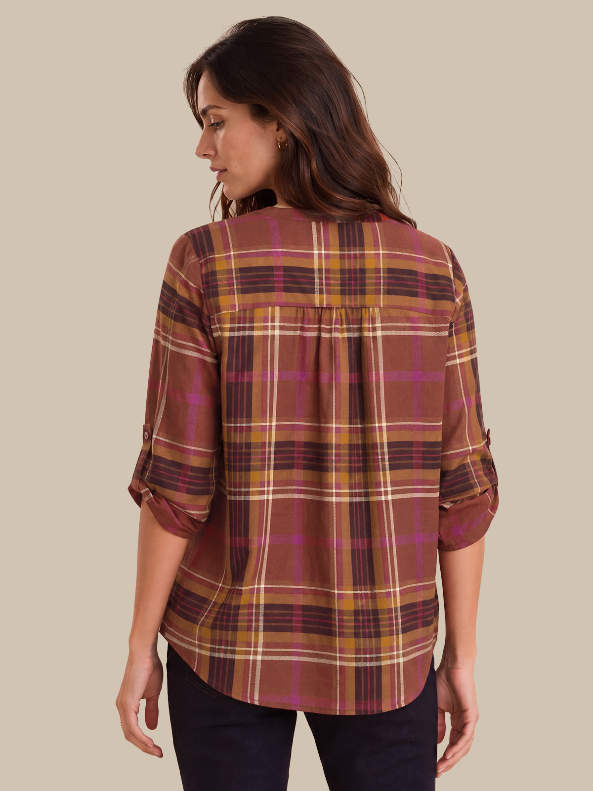 A woman shown from the back wearing a plaid button-up shirt with three-quarter sleeves, featuring a pattern of rust brown, mustard yellow, and magenta on a beige background.