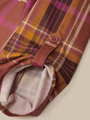 Close-up of a plaid button-up shirt sleeve in warm autumn tones, featuring brown, orange, purple, and beige stripes with a visible button and turned-back cuff showing the light lining.