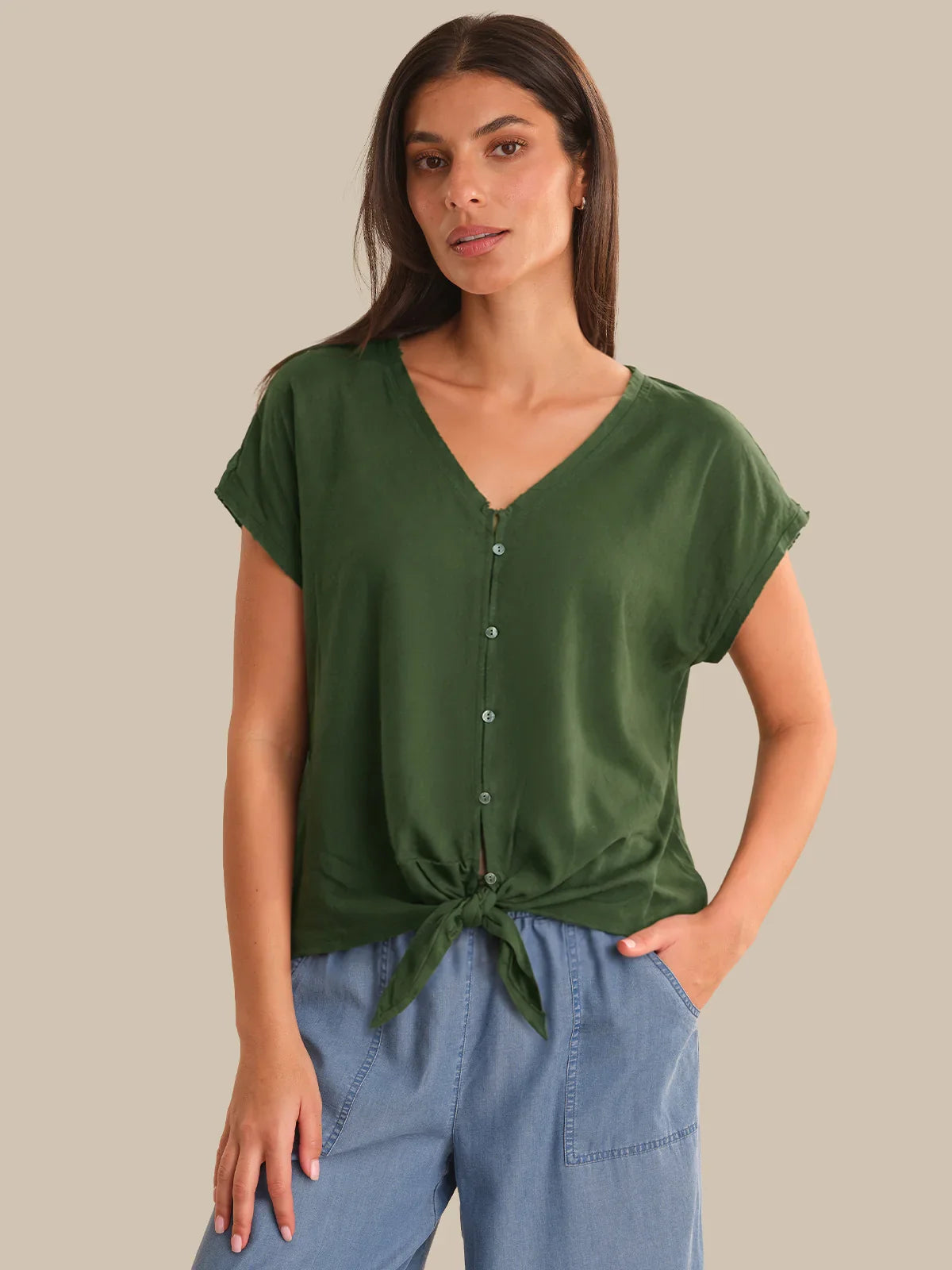 Woman wearing a green top with a tie detail and blue pants on a beige background