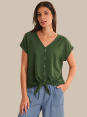 Woman wearing a green top with a tie detail and blue pants on a beige background