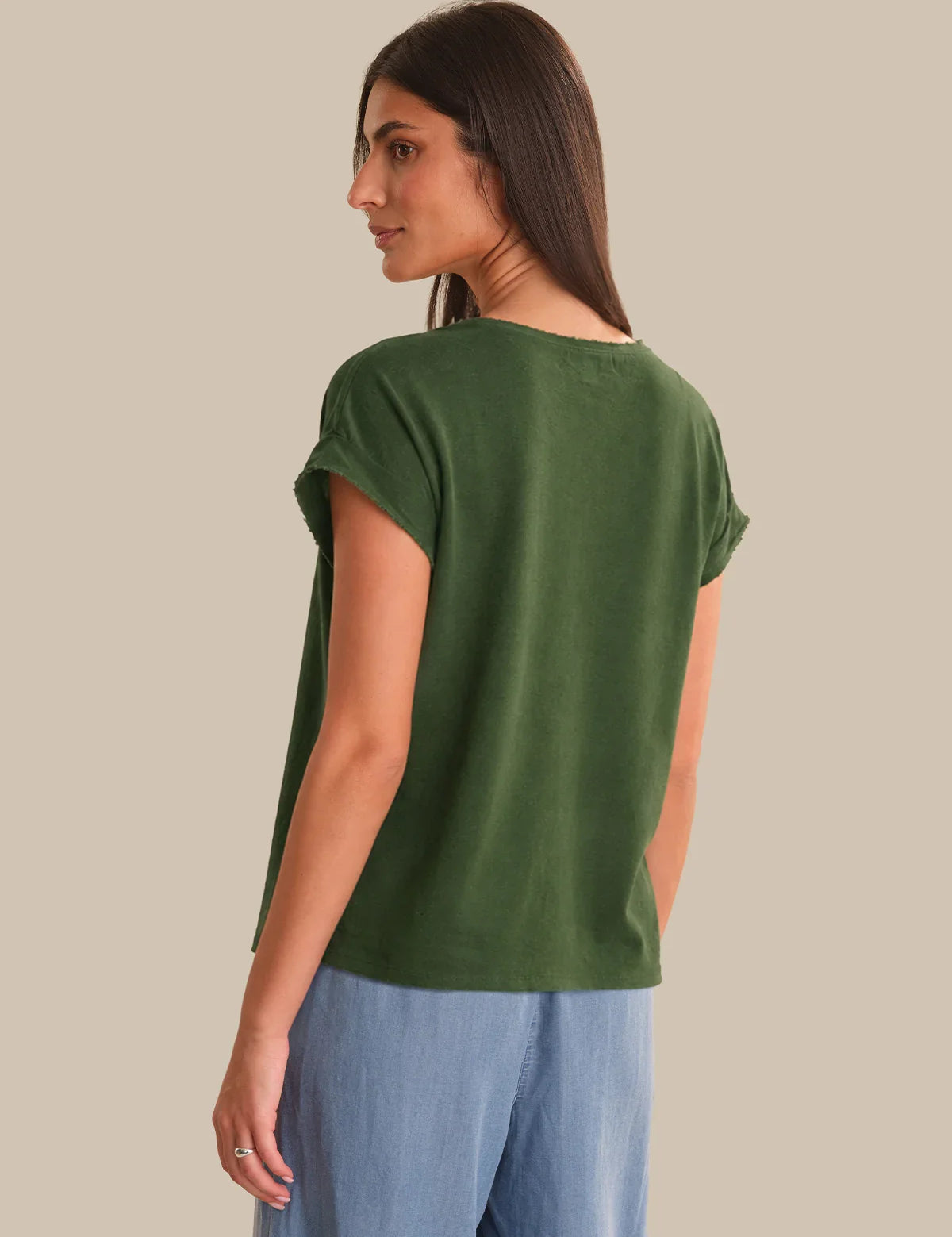 Woman wearing a green t-shirt and blue pants on a beige background
