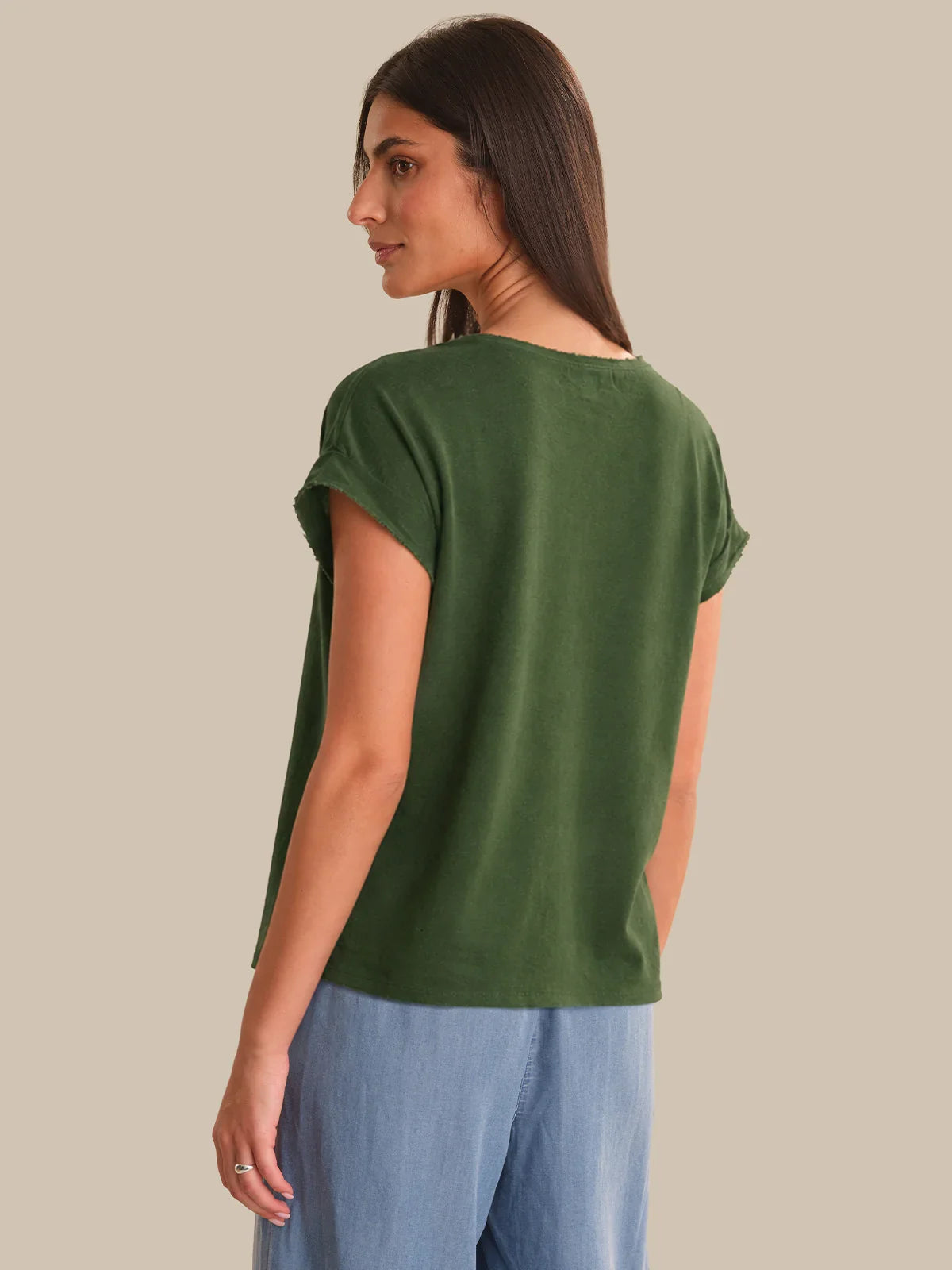 Woman wearing a green t-shirt and blue pants on a beige background