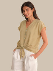 Woman wearing a beige top with a tie detail and white pants on a plain background