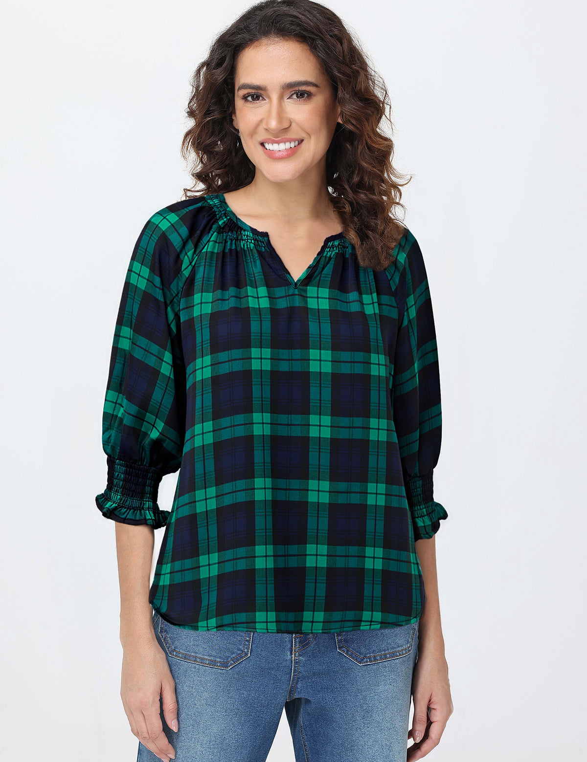 Woman wearing a green and navy plaid blouse with blue jeans on a white background