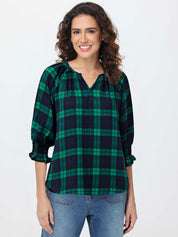 Woman wearing a green and navy plaid blouse with blue jeans on a white background