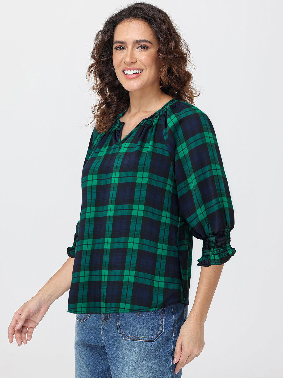 Woman wearing a green and navy plaid shirt with blue jeans on a white background