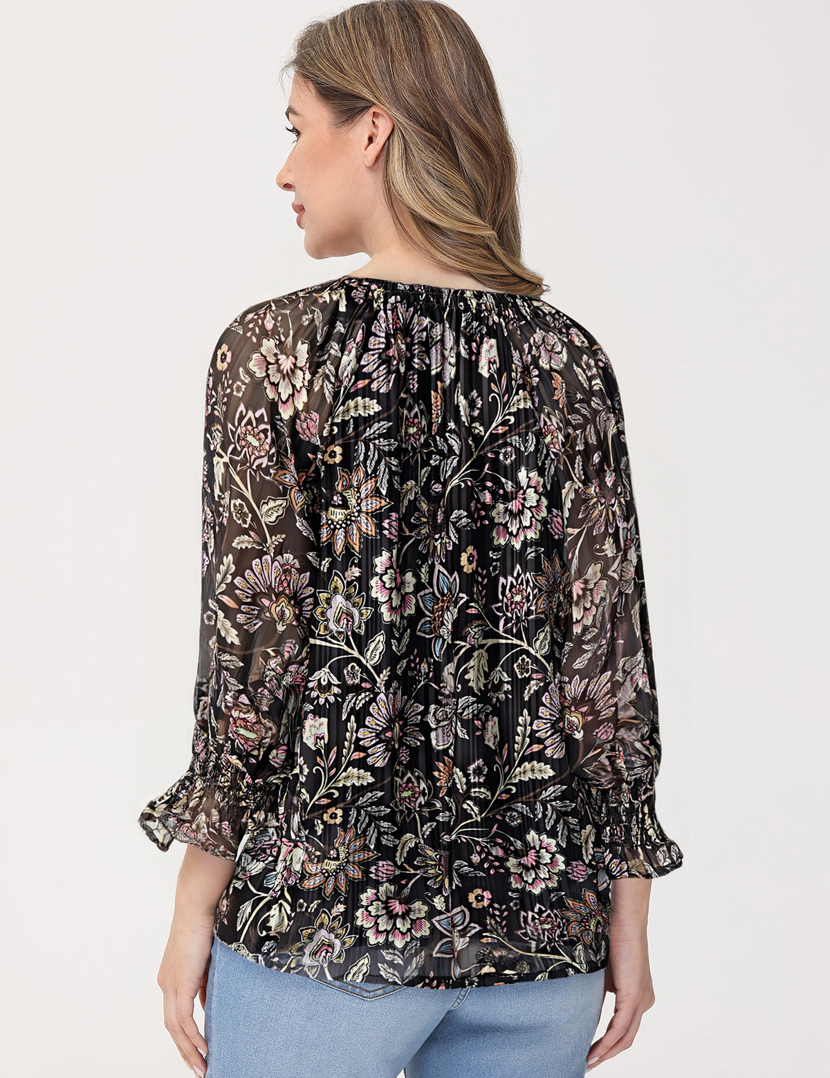 Woman wearing a black floral blouse with light blue jeans on a white background