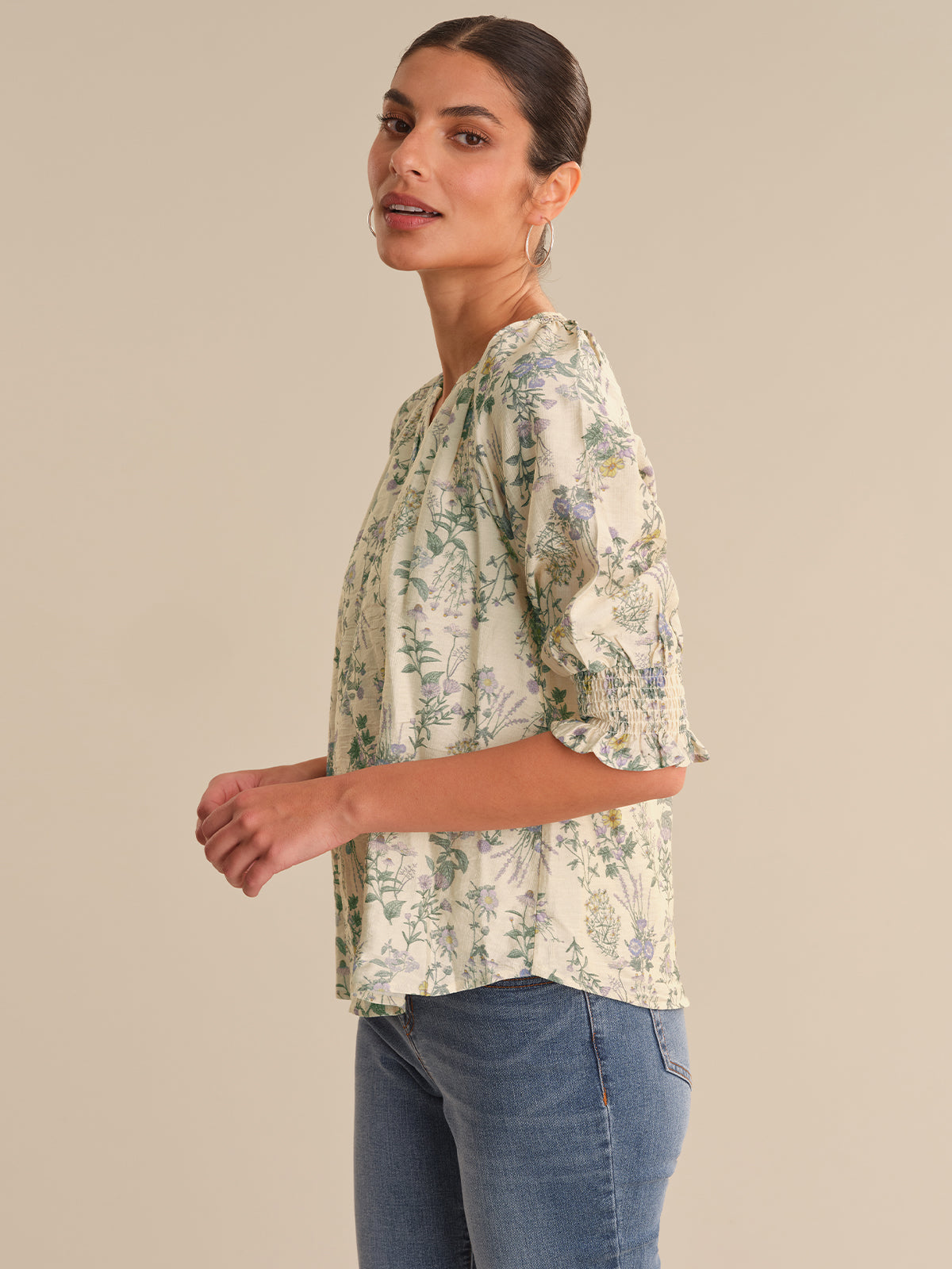 Woman wearing a floral blouse and jeans on a beige background