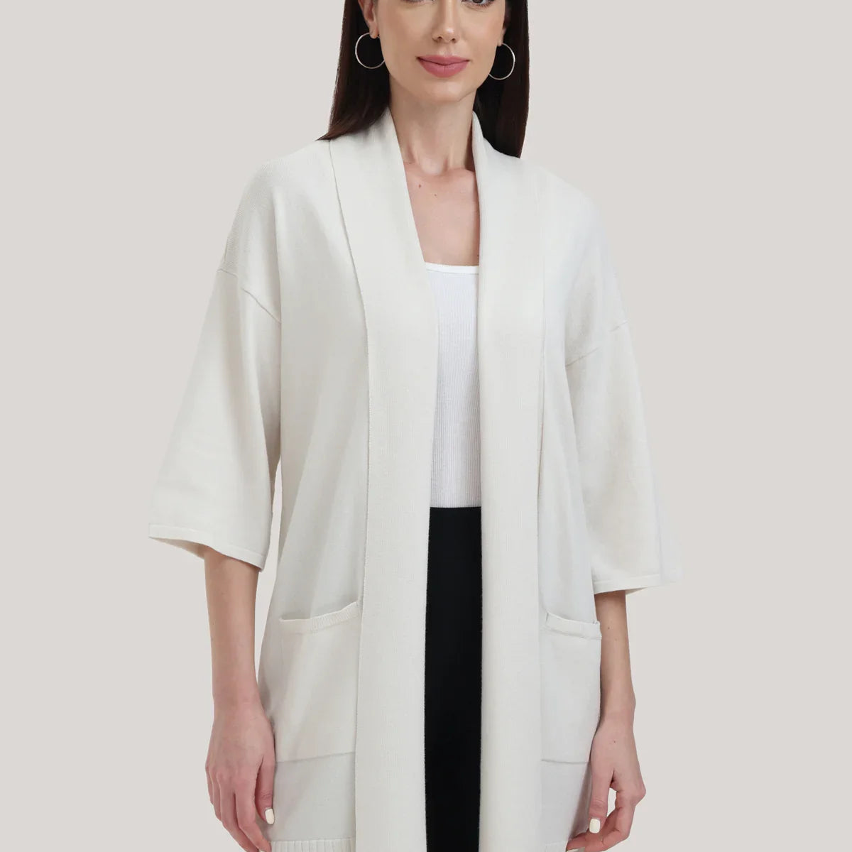 Woman wearing a white kimono-style cardigan over a black outfit on a plain background