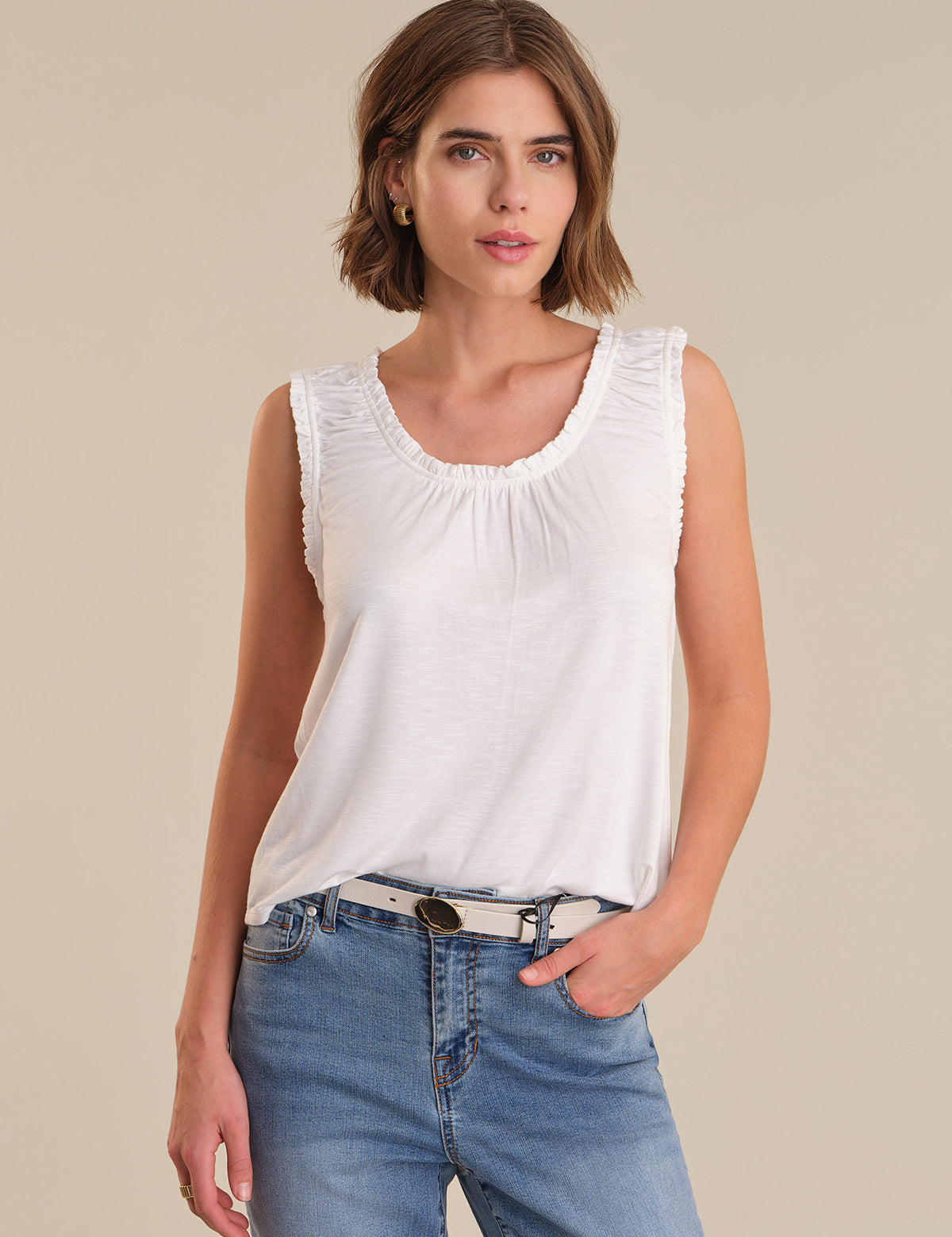 Woman wearing a white sleeveless top and blue jeans on a beige background
