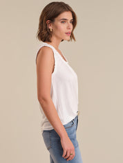 Woman wearing a white sleeveless top and blue jeans on a beige background