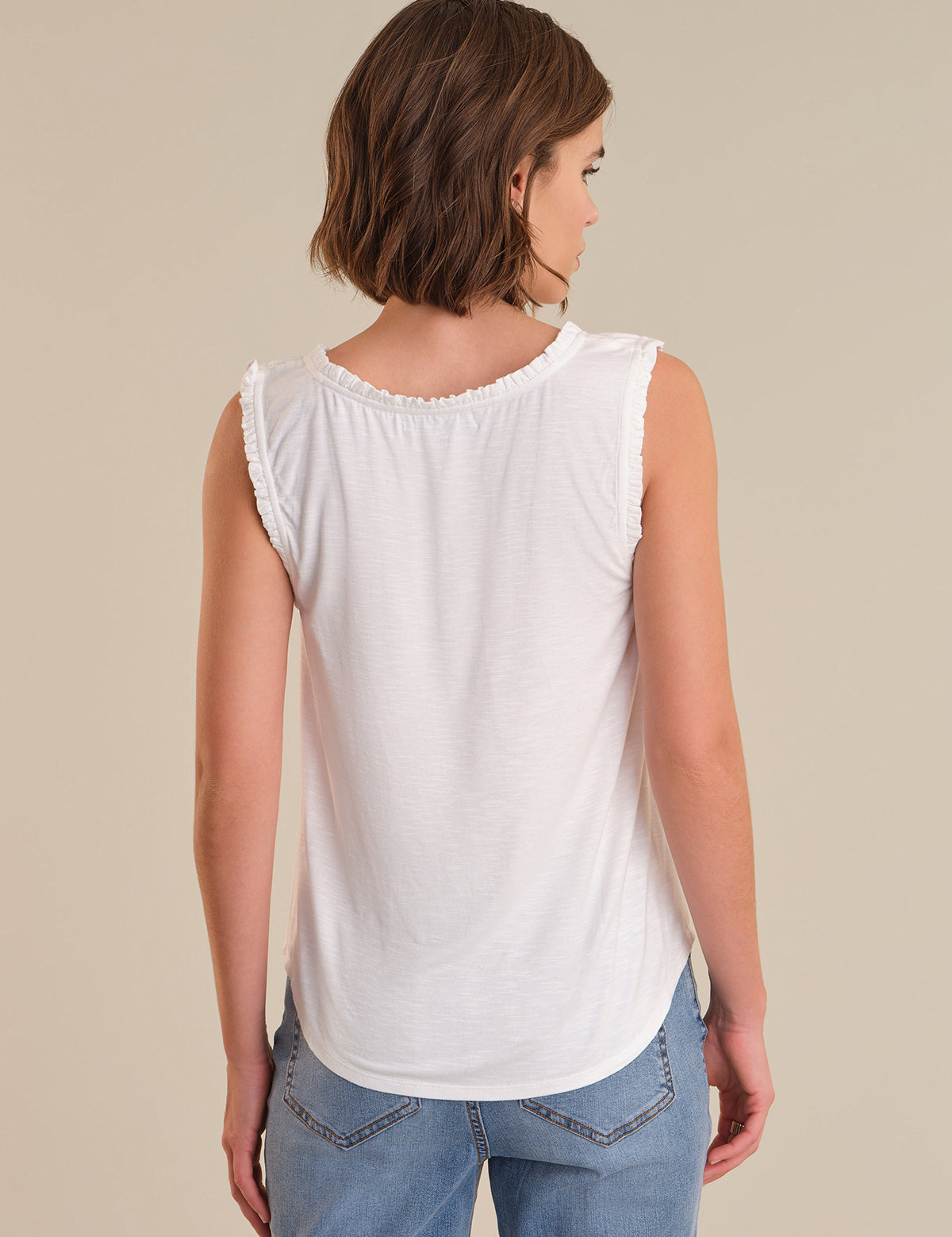 Woman wearing a white sleeveless top and blue jeans on a beige background