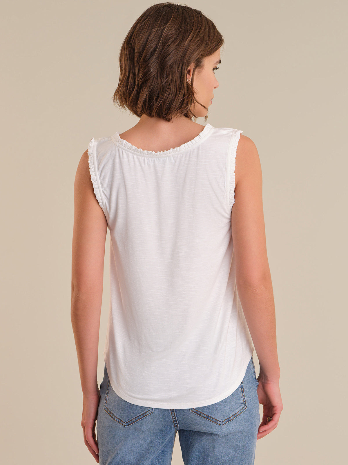 Woman wearing a white sleeveless top and blue jeans on a beige background