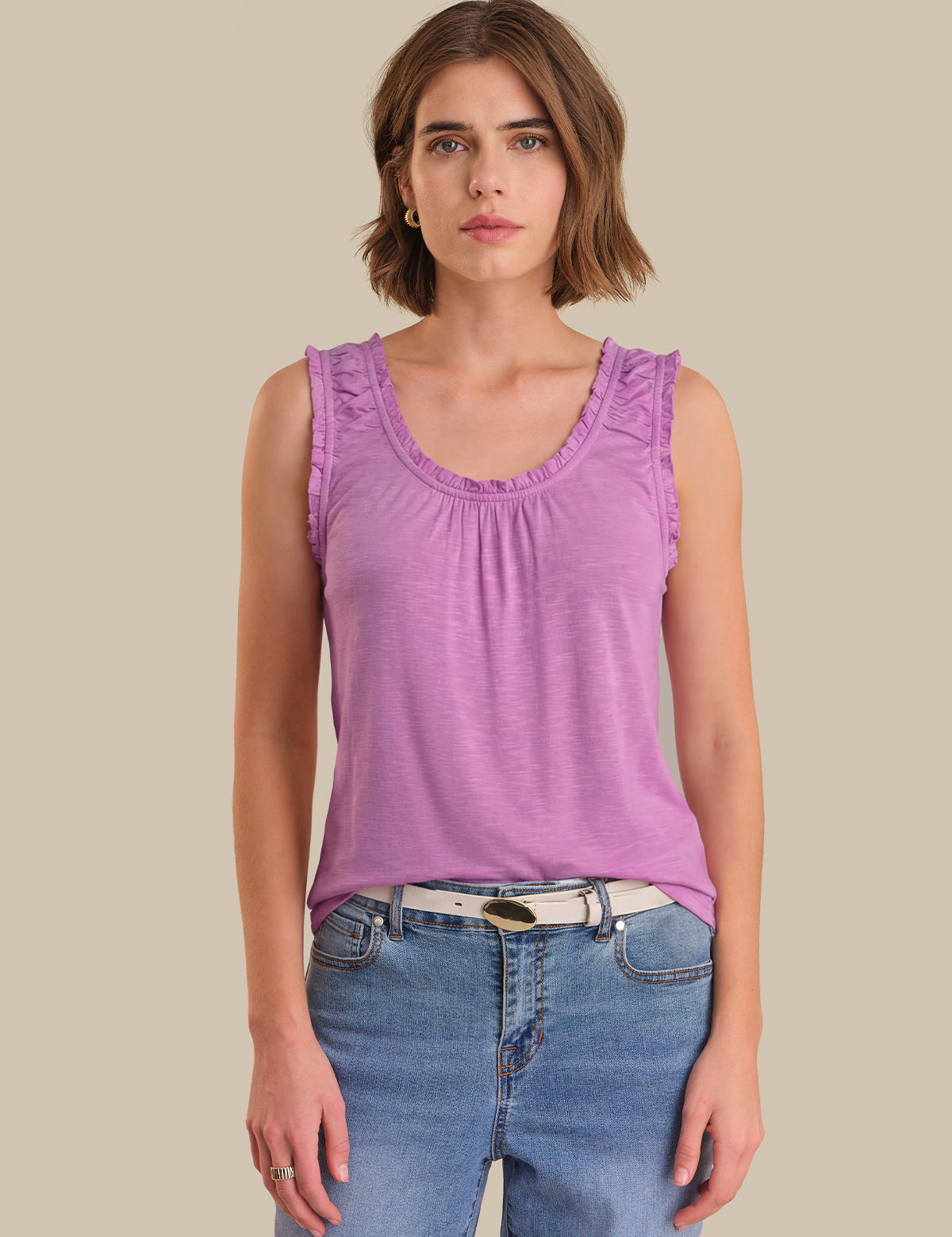 Woman wearing a purple tank top and blue jeans against a beige background