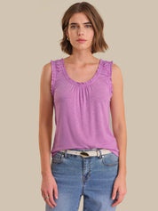 Woman wearing a purple tank top and blue jeans against a beige background