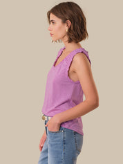 Woman wearing a purple sleeveless top and blue jeans against a beige background