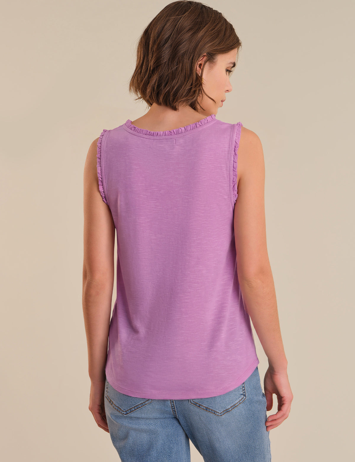 Woman wearing a purple sleeveless top and blue jeans on a beige background